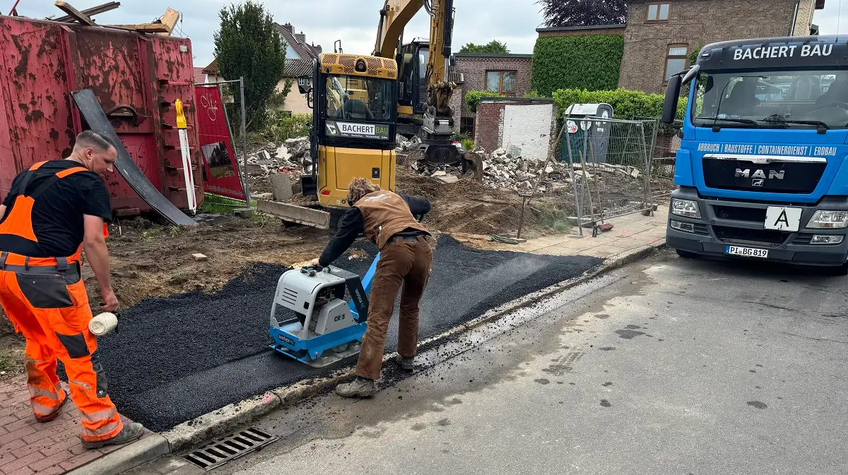 Asphaltierung einer Baustellenüberfahrt durch Bachert Bau Baustellenüberfahrt aus Heißasphalt in Hamburg – Bachert Bau beim Asphaltieren mit Rüttelplatte und Bagger.“